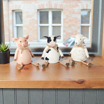Pig, cow and sheep farm animal shelf sitter ornaments in neutral country style, sitting on a wooden windowsill with dangling legs