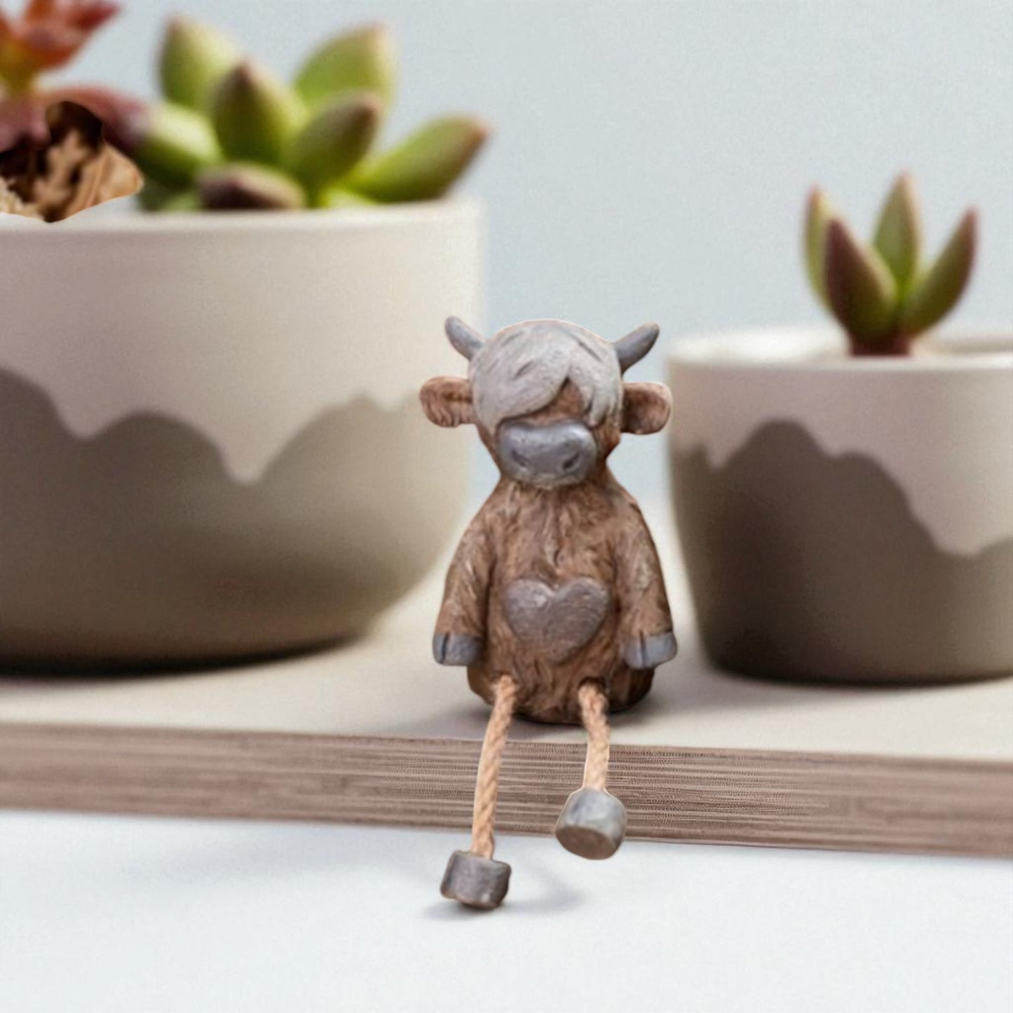 Highland cow shelf sitter ornament with dangling legs on wooden shelf
